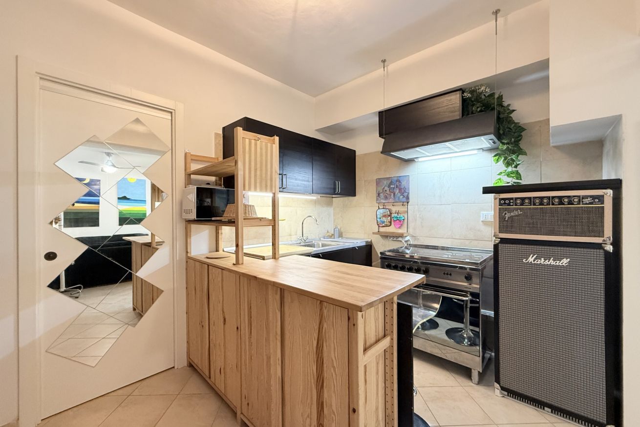 Una cocina compacta con barra de madera, microondas integrado, estufa y un amplificador Marshall.