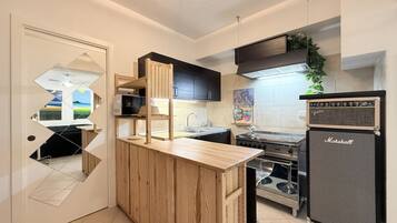 Una cocina compacta con barra de madera, microondas integrado, estufa y un amplificador Marshall.