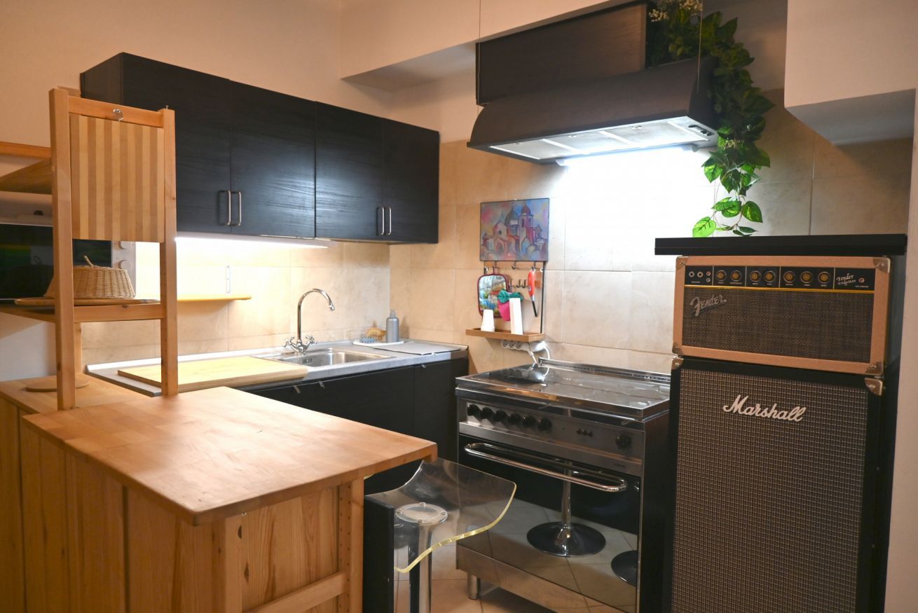 A compact kitchen with dark cabinets, a wooden countertop, a stove, and a Marshall amplifier.