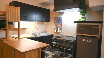 A compact kitchen with dark cabinets, a wooden countertop, a stove, and a Marshall amplifier.
