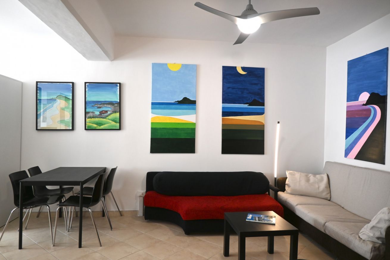 Un salon moderne avec un canapé noir, un plaid rouge, une table à manger avec des chaises et trois tableaux accrochés au mur.