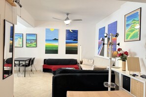 A modern living room with a black sofa, a dining table, and chairs. There are paintings on the walls and a ceiling fan. - Molevan 1 – Ancona, bright and fully equipped studio apartment close to all amenities (Ancona)