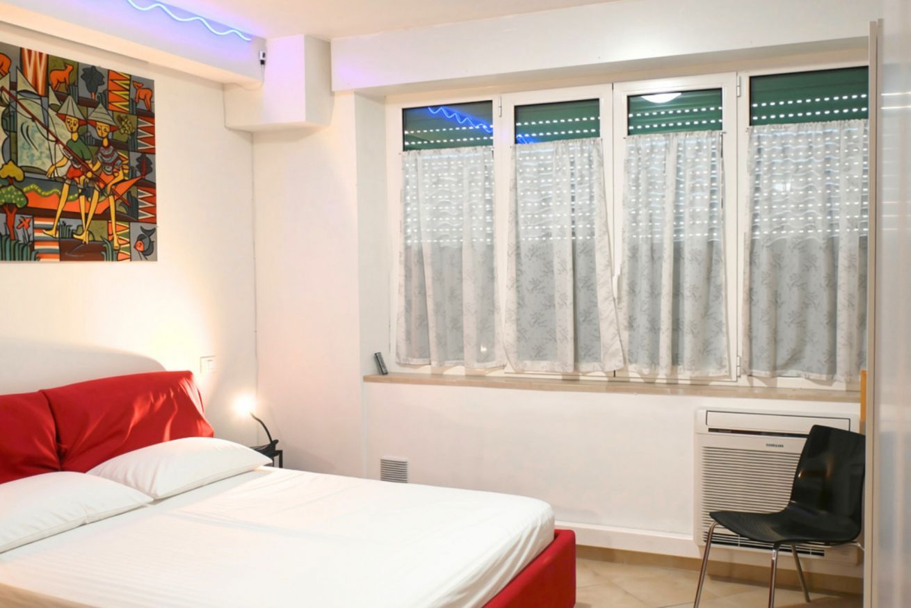A bedroom with a bed, a chair, a radiator, and a window with curtains.