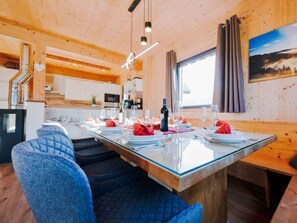 A dining area with a glass-top table, blue upholstered chairs, and a view of the kitchen and outdoors. - One-bedroom Cabin (Sankt Georgen am Kreischberg)