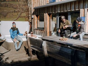 A wooden deck with a hot tub and a table with people sitting around. - One-bedroom Cabin (Sankt Georgen am Kreischberg)