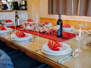 A dining table set with plates, cutlery, glasses, and a bottle of wine, with a red table runner and decorative flowers. - One-bedroom Cabin (Sankt Georgen am Kreischberg)