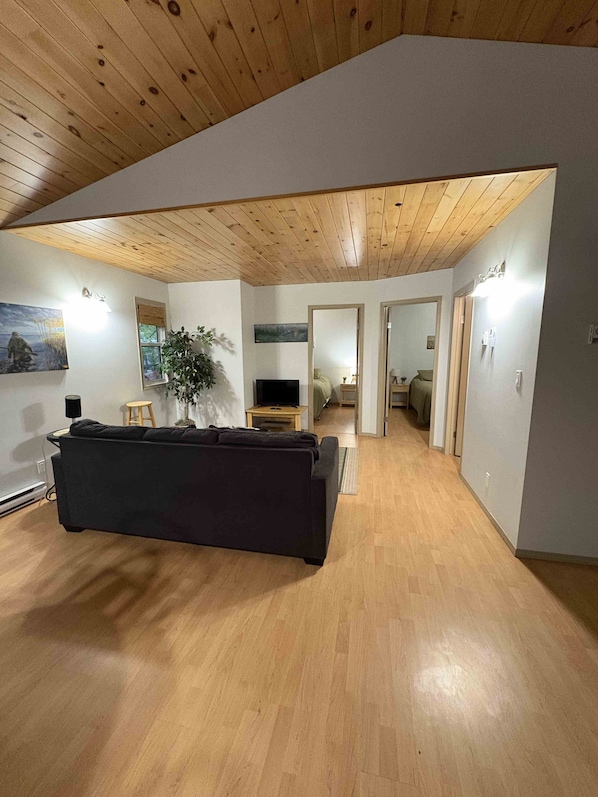 A living room with a dark sofa, wooden flooring, and a ceiling with wooden beams.