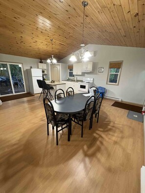 Una cocina amplia con armarios blancos, una mesa de comedor con sillas y techo de madera.
