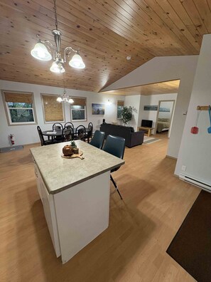 Eine moderne Küche mit Kochinsel, Essbereich mit Stühlen, einer Couch und einem Fernseher im Hintergrund.