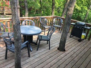 A deck with a round table and chairs, surrounded by trees. - Large Cabin Super Close to Oak Lake! Perfect for Duck Hunting and Ice Fishing! (Oak Lake Beach)