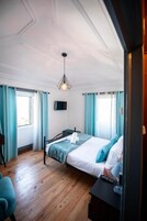 Un dormitorio con cama, escritorio, silla, televisor y ventana con cortinas.