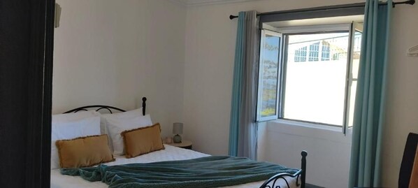 Une chambre à coucher avec un lit, des oreillers, une table de chevet, une lampe et une fenêtre avec des rideaux.
