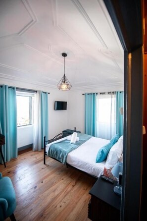 Een slaapkamer met een bed, een bureau, een stoel, een televisie en een raam met gordijnen.