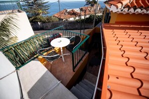 Een balkon met een tafel en stoelen, uitzicht op de zee en een pannendak.