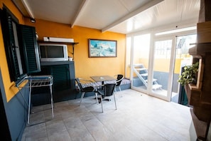 Un espace patio aménagé avec une table et des chaises, un four à micro-ondes, un tableau accroché au mur et une porte-fenêtre coulissante donnant sur un espace extérieur.