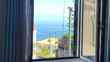 Une chambre dotée d’une grande fenêtre, d’un lit et offrant une vue sur la mer.