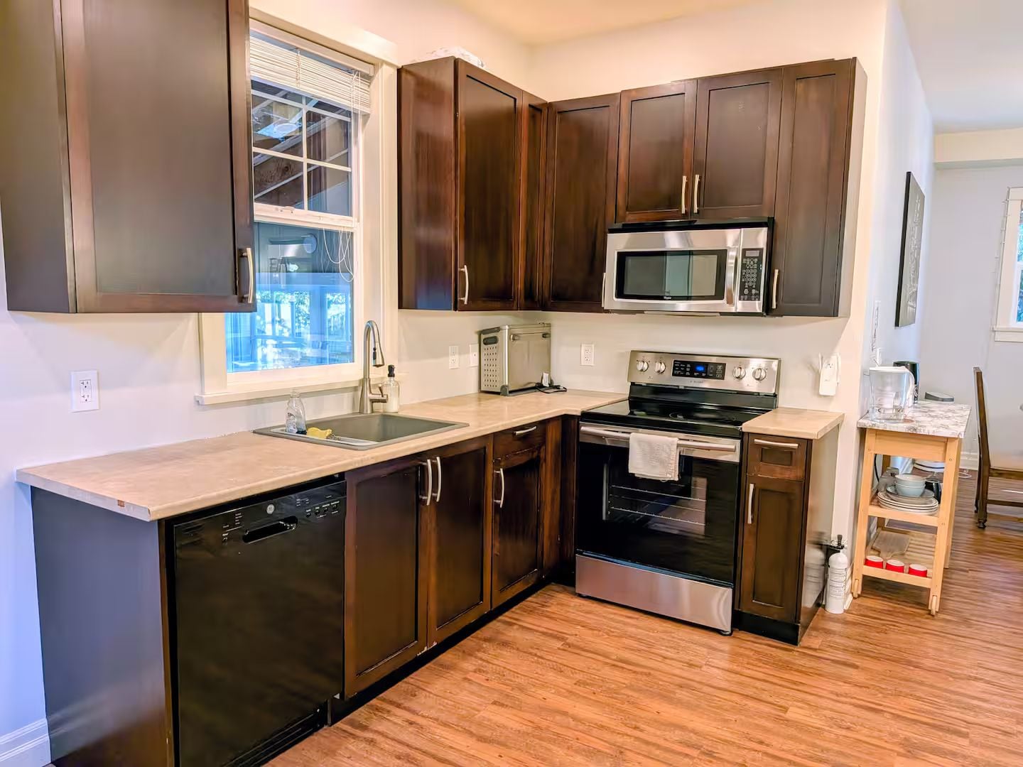 A modern kitchen with dark wood cabinets, stainless steel appliances, and a wooden floor.