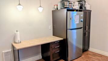 Una cocina compacta con refrigerador empotrado, una encimera con dispensador de toallas de papel y un pequeño banco.