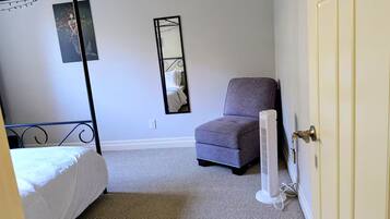 A bedroom with a four-poster bed, a chair, a standing heater, and a mirror on the wall.