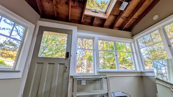 A room with a wooden ceiling, large windows, and a shoe rack.