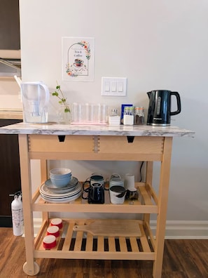 Una encimera de cocina con una cafetera, una jarra de agua y diversos utensilios de cocina.