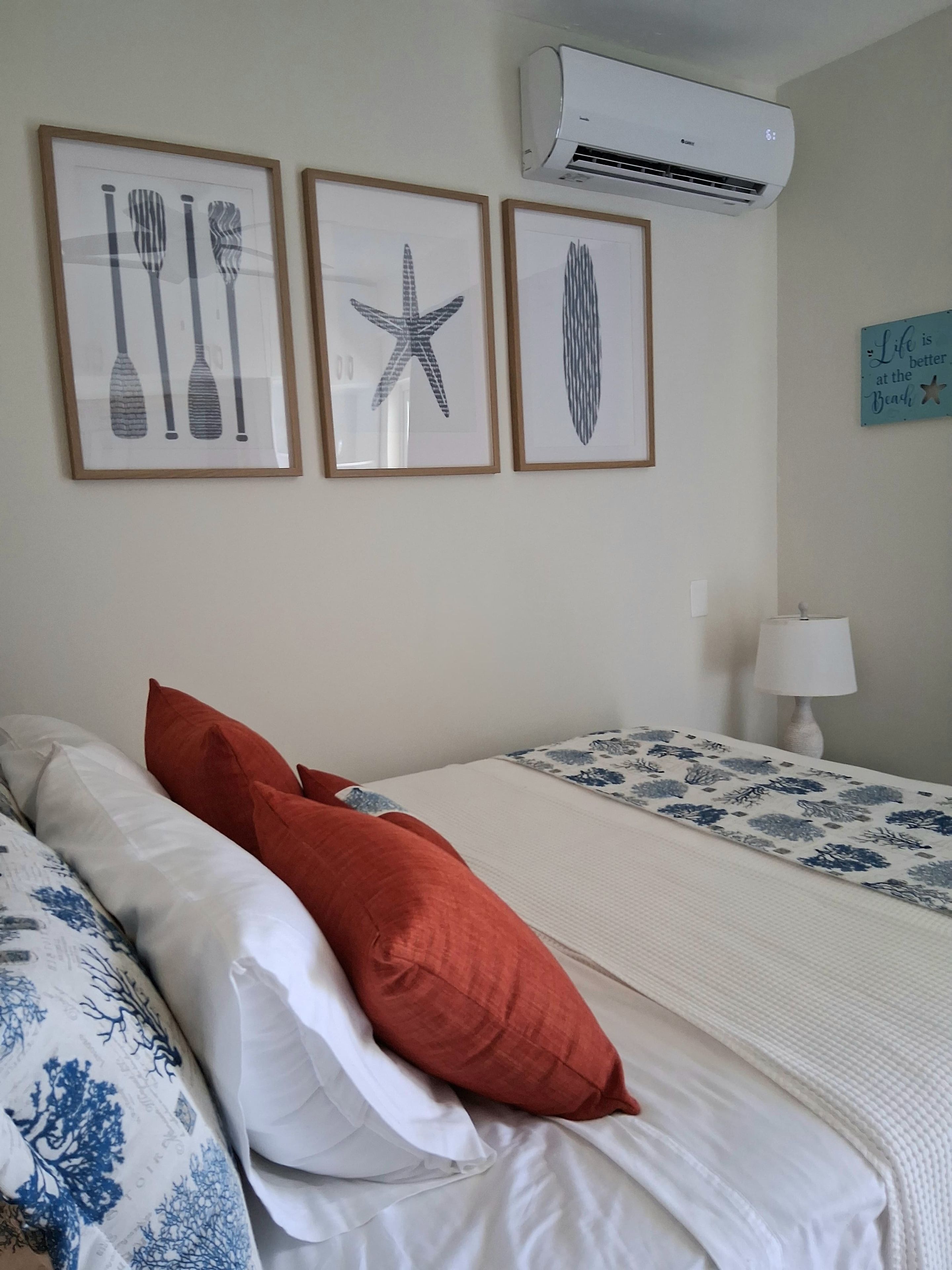 Een slaapkamer met een bed, kussens, een nachtkastje, een lamp en wanddecoratie.