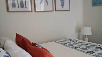 Een slaapkamer met een bed, kussens, een nachtkastje, een lamp en wanddecoratie.