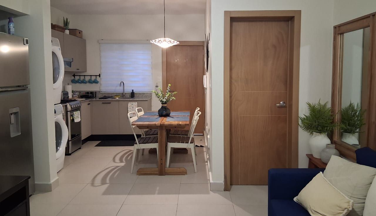 Un espacio habitable pequeño con zona de comedor, kitchenette y un sofá azul.