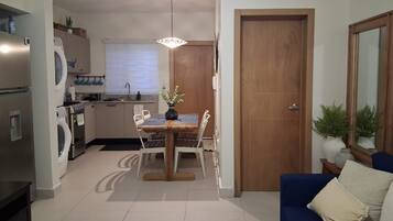 Un espacio habitable pequeño con zona de comedor, kitchenette y un sofá azul.