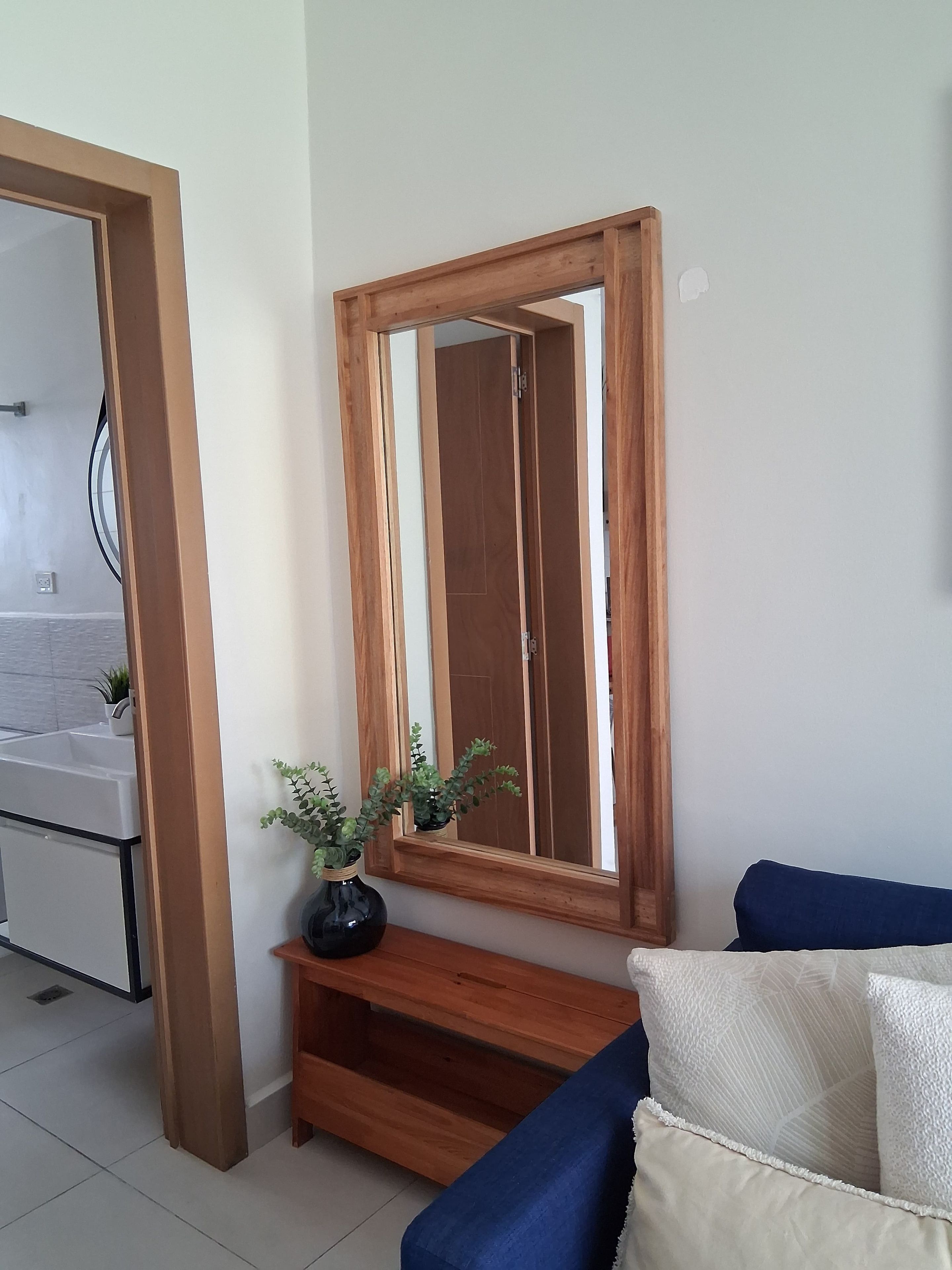 Una habitación con un espejo de marco de madera, un sofá azul y una planta pequeña sobre una consola de madera.
