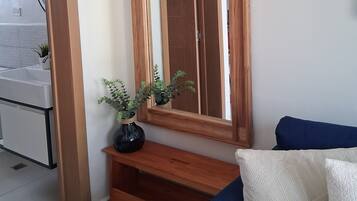 Una habitación con un espejo de marco de madera, un sofá azul y una planta pequeña sobre una consola de madera.