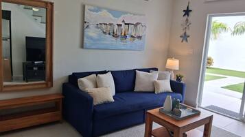 A living room with a blue sofa, a coffee table, a painting of boats, a star decoration, and a large window.