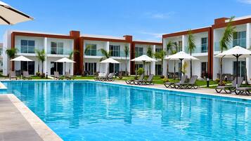 Un hotel moderno con piscina, tumbonas y palmeras.