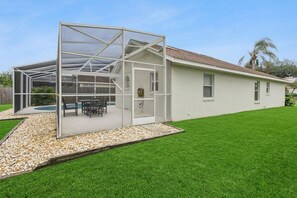 Ein Haus mit überdachter Terrasse, Swimmingpool und gepflegtem Rasen.