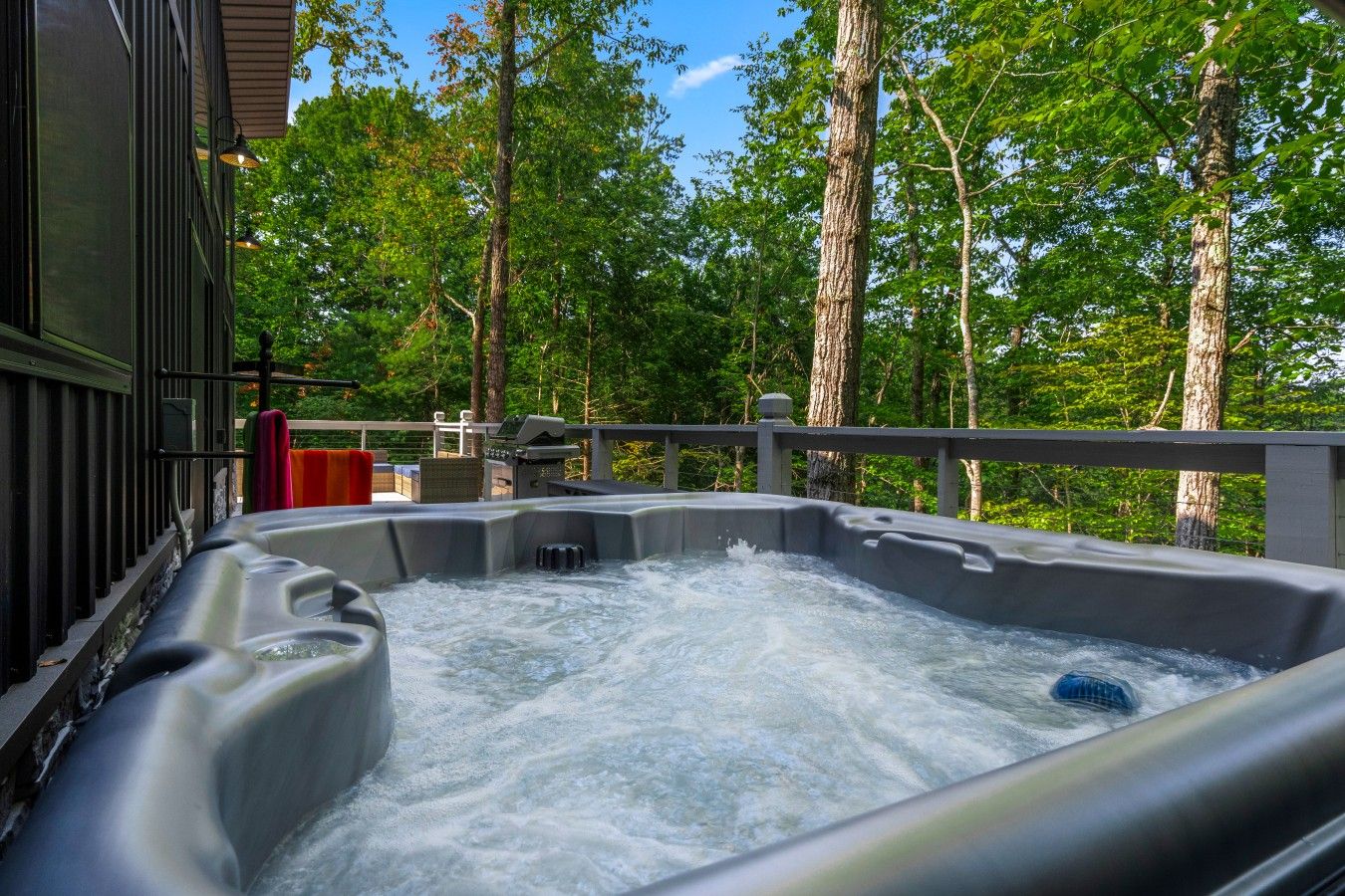Un bain à remous doté d’une cascade, entouré d’arbres et agrémenté d’une terrasse en bois.