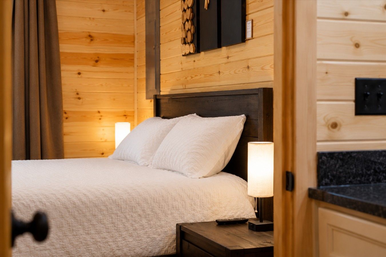 A wooden room with a bed, nightstands, and a wall-mounted shelf with logs.