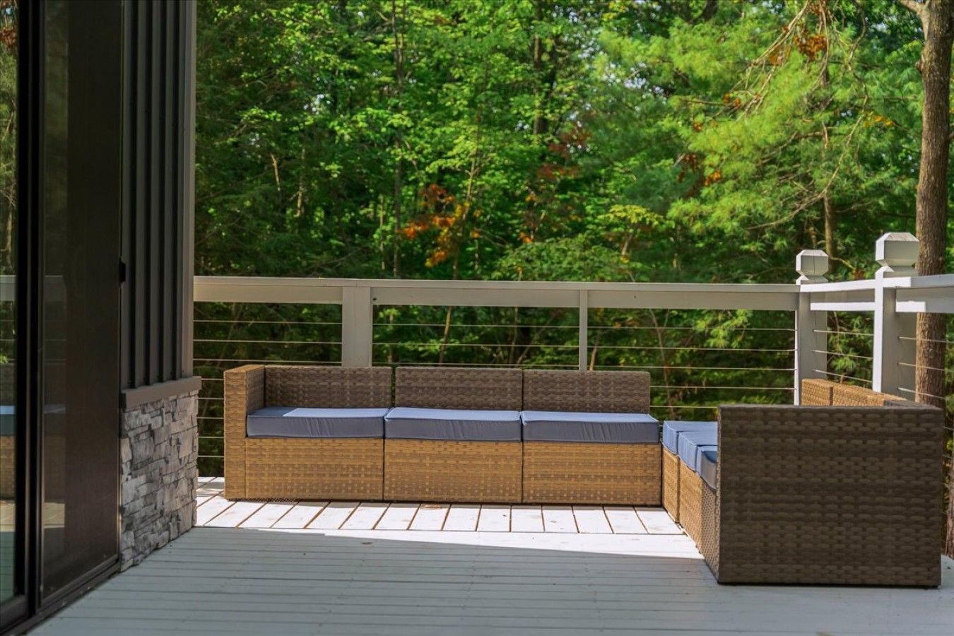 Una terraza exterior con un sofá de mimbre y un sillón a juego, una pared de piedra y una barandilla blanca.