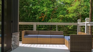Una terraza exterior con un sofá de mimbre y un sillón a juego, una pared de piedra y una barandilla blanca.
