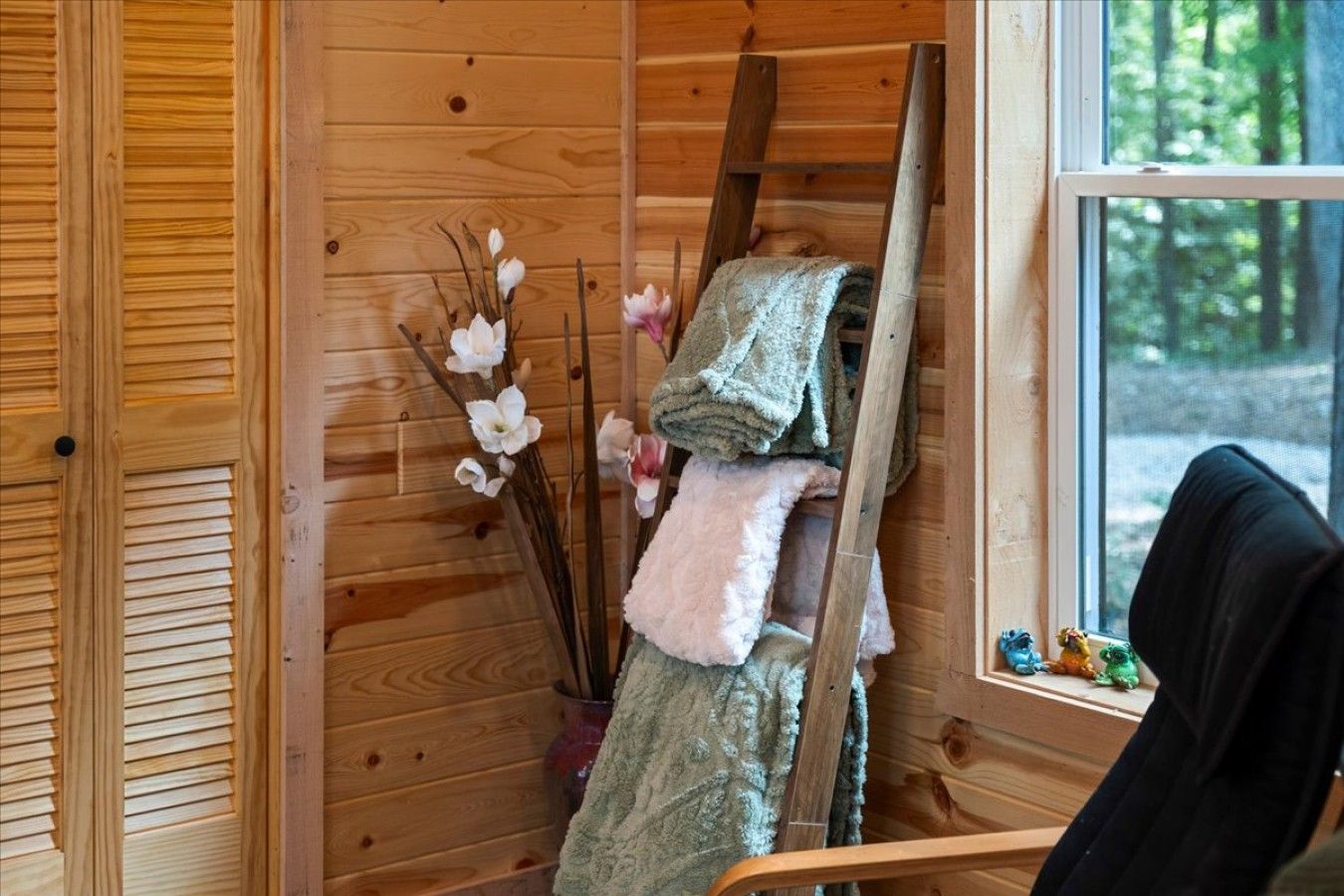 Interior de una cabaña de madera con ventana, escalera y una silla.