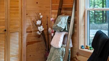 Interior de una cabaña de madera con ventana, escalera y una silla.