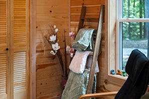 Interior de una cabaña de madera con ventana, escalera y una silla.