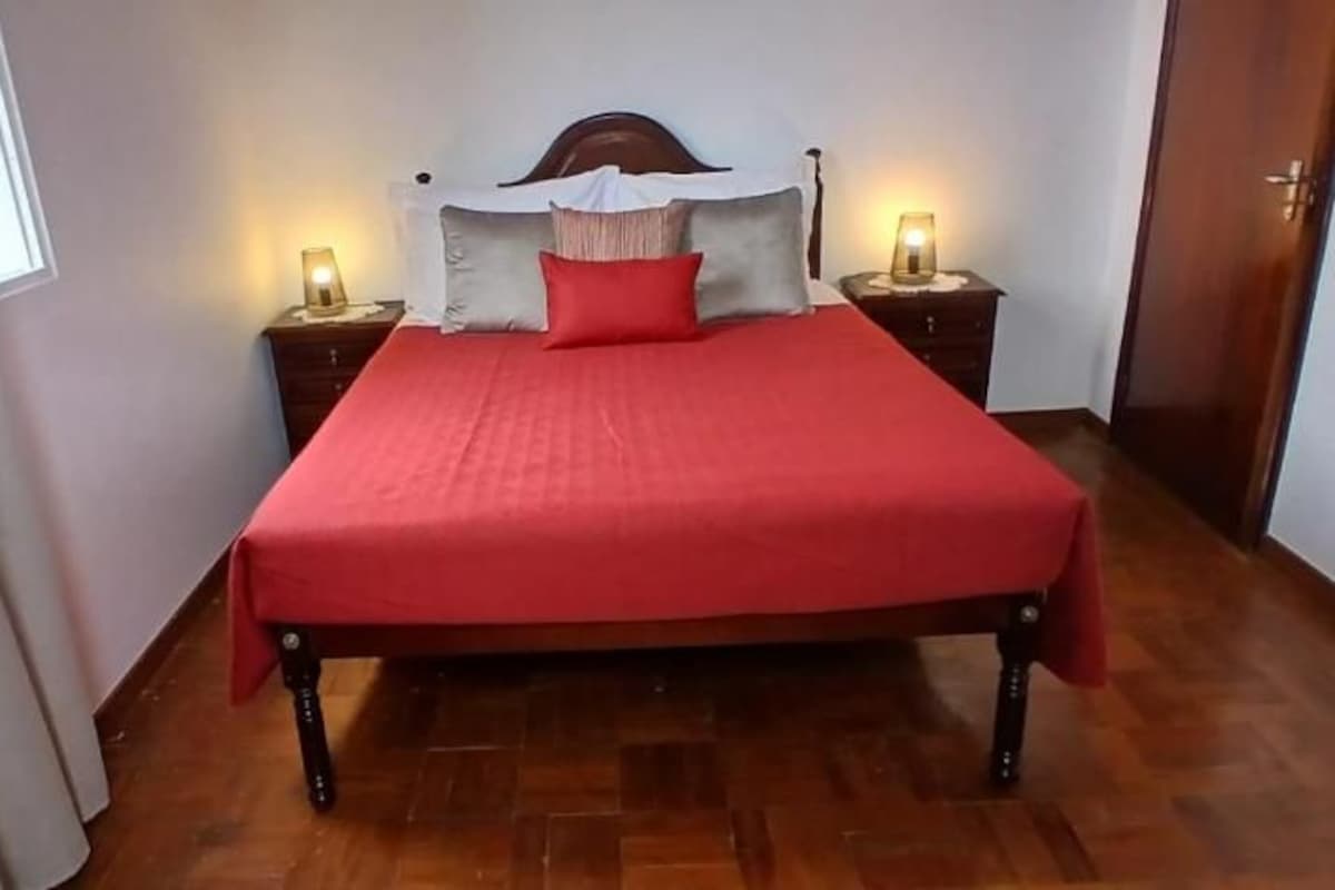 A bed with a red bedspread, two bedside tables with lamps, and a wooden floor.
