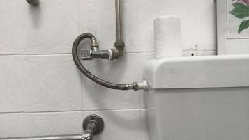 Een badkamer met witte betegelde wanden, een toilet, een handgreep en een douche slang.