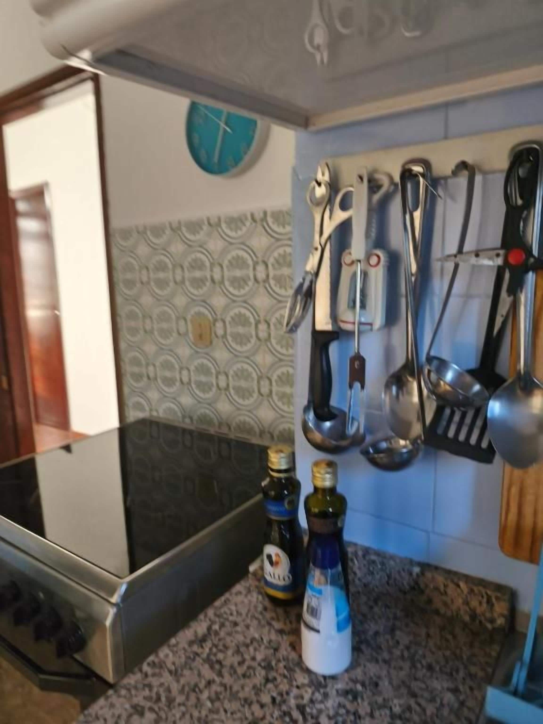 A kitchen with a stove, two bottles of olive oil, and a clock on the wall.