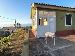 A small building with a door and windows, a small table, and a garden area with plants. - Três Marias (Porto Moniz)
