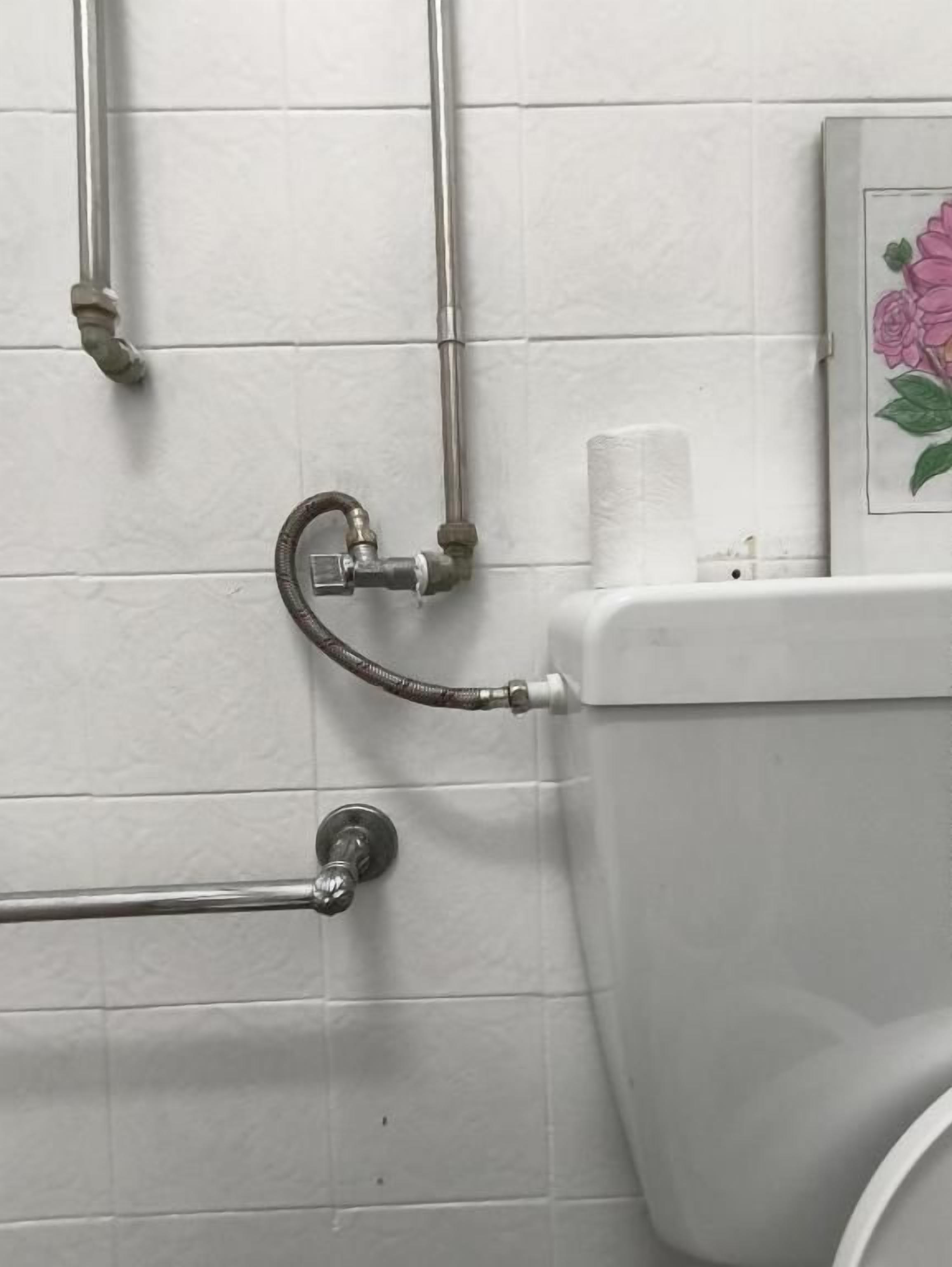 Une salle de bain avec des murs carrelés de carreaux blancs, des toilettes, une barre d’appui et un flexible de douche.