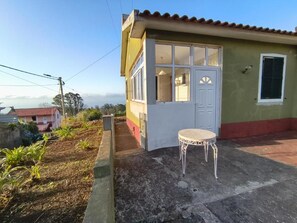 A small house with a white door and windows, a concrete patio, and a small round table.