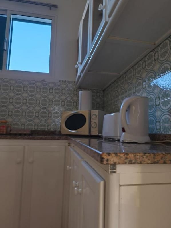A kitchen with a microwave, toaster, and kettle on the counter, with patterned backsplash and cabinets.