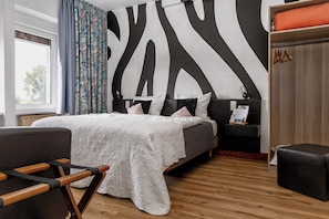 A modern bedroom with a large bed, a wooden floor, a zebra-patterned wall, and a window with curtains.