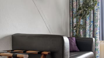 Een moderne woonkamer met een leren bank, een houten salontafel, een flatscreen televisie aan de muur en een potplant.